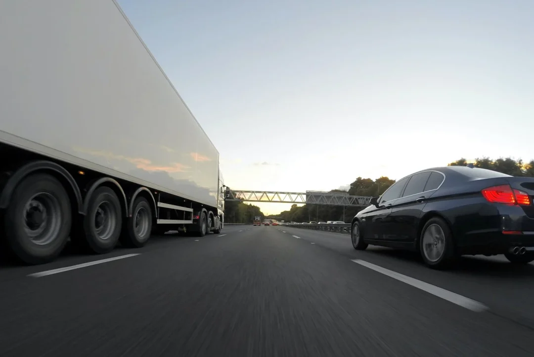 A truck and a car are driving on an fast road.